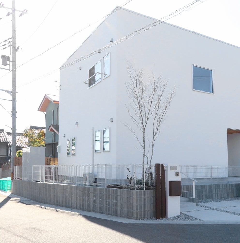 白い外壁の家。壁を伝う竪樋と、コンクリートと砂利で仕上げた足元（奈良県内・シバ・サンホームの施工例）